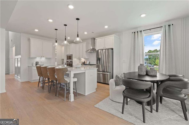 kitchen with a center island with sink, white cabinetry, wall chimney range hood, and stainless steel fridge with ice dispenser