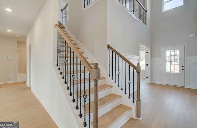 foyer entrance featuring a wainscoted wall, recessed lighting, light wood-style floors, a towering ceiling, and a decorative wall