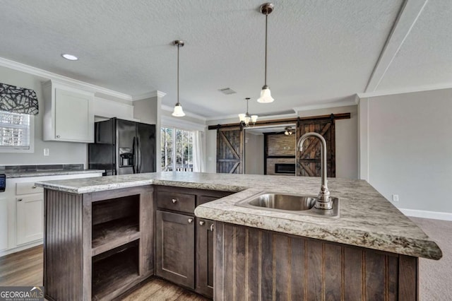 kitchen with black fridge with ice dispenser, sink, white cabinetry, a center island with sink, and a barn door