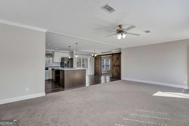 unfurnished living room with crown molding, ceiling fan, a barn door, and dark colored carpet