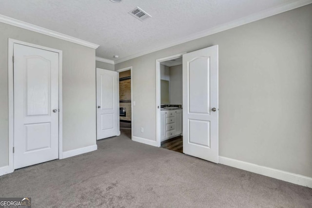 unfurnished bedroom with dark colored carpet, ornamental molding, ensuite bathroom, and a textured ceiling