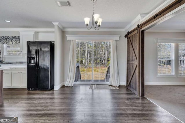 unfurnished dining area with dark wood-type flooring, a textured ceiling, ornamental molding, a notable chandelier, and a barn door