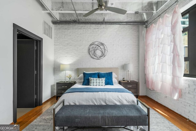 bedroom featuring ceiling fan, brick wall, and hardwood / wood-style floors