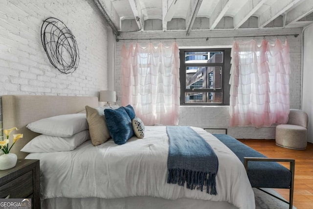 bedroom with hardwood / wood-style floors and brick wall