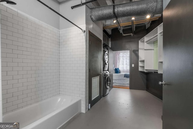 bathroom with concrete flooring, tiled shower / bath, and stacked washer / dryer