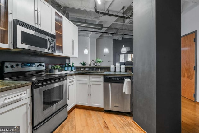 kitchen with sink, white cabinetry, hanging light fixtures, stainless steel appliances, and light hardwood / wood-style floors