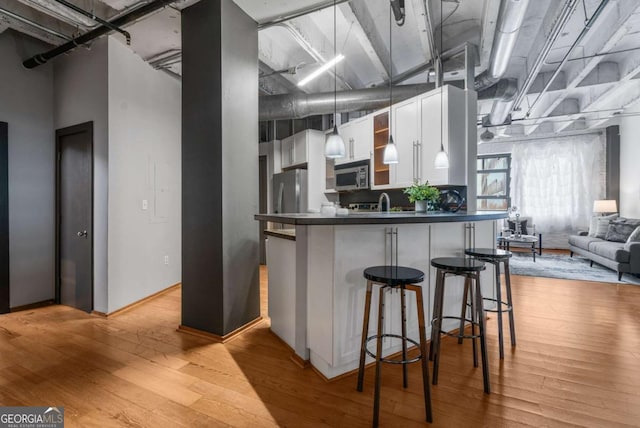 kitchen with a breakfast bar area, appliances with stainless steel finishes, light hardwood / wood-style floors, white cabinets, and kitchen peninsula