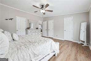 bedroom featuring ceiling fan, ornamental molding, hardwood / wood-style floors, and two closets