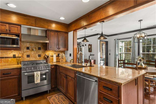 kitchen with decorative light fixtures, sink, kitchen peninsula, stainless steel appliances, and wall chimney range hood