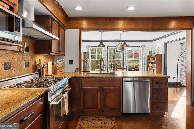 kitchen featuring sink, light stone counters, appliances with stainless steel finishes, pendant lighting, and wall chimney range hood