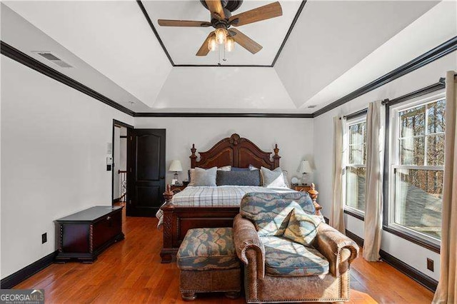 bedroom featuring a raised ceiling, crown molding, wood-type flooring, and ceiling fan