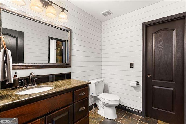 bathroom featuring vanity, wooden walls, and toilet