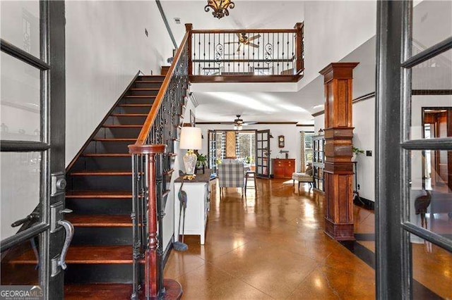 staircase with a high ceiling, ceiling fan, and ornate columns