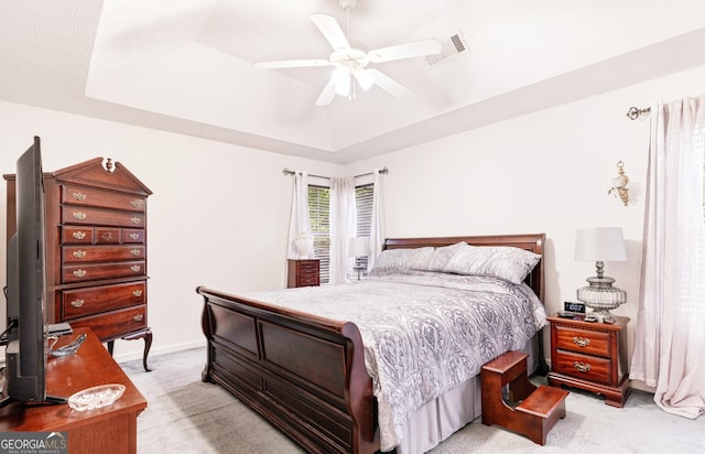 bedroom featuring light carpet, a tray ceiling, and ceiling fan