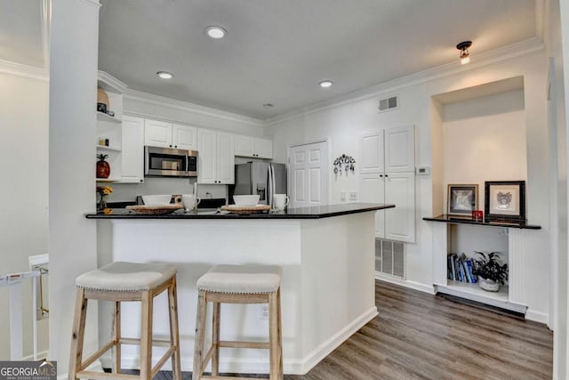 kitchen with hardwood / wood-style floors, white cabinets, ornamental molding, kitchen peninsula, and stainless steel appliances