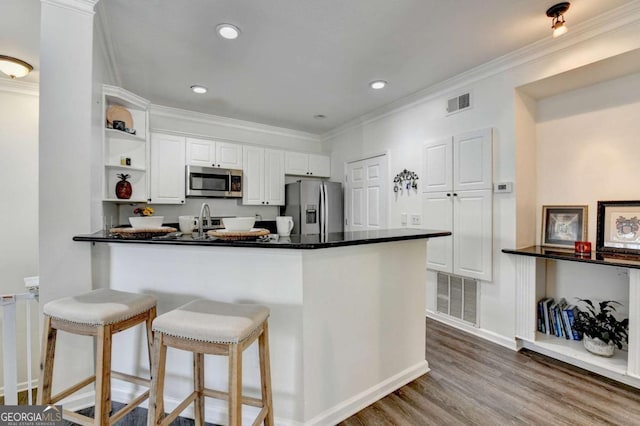 kitchen with white cabinetry, crown molding, appliances with stainless steel finishes, kitchen peninsula, and hardwood / wood-style floors