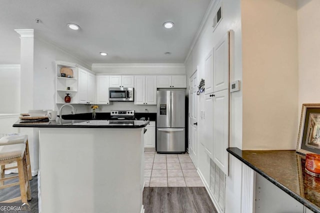 kitchen with light tile patterned flooring, white cabinets, ornamental molding, kitchen peninsula, and stainless steel appliances