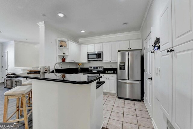 kitchen with stainless steel appliances, white cabinetry, a breakfast bar, and kitchen peninsula