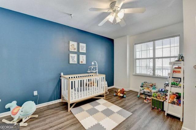 bedroom featuring hardwood / wood-style flooring, ceiling fan, and a crib