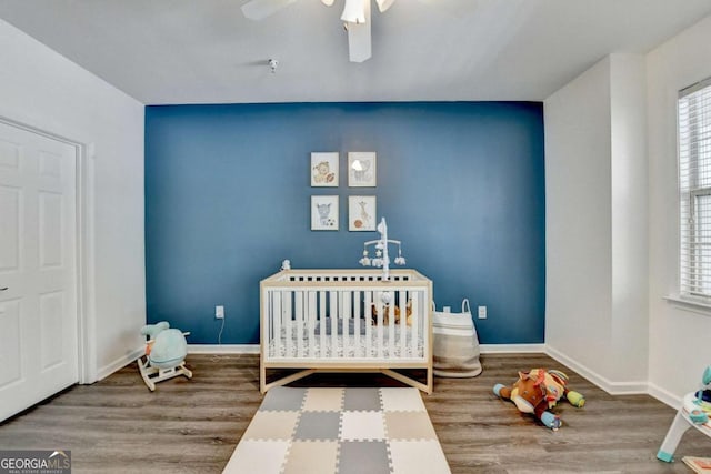 bedroom featuring a nursery area, ceiling fan, and wood-type flooring