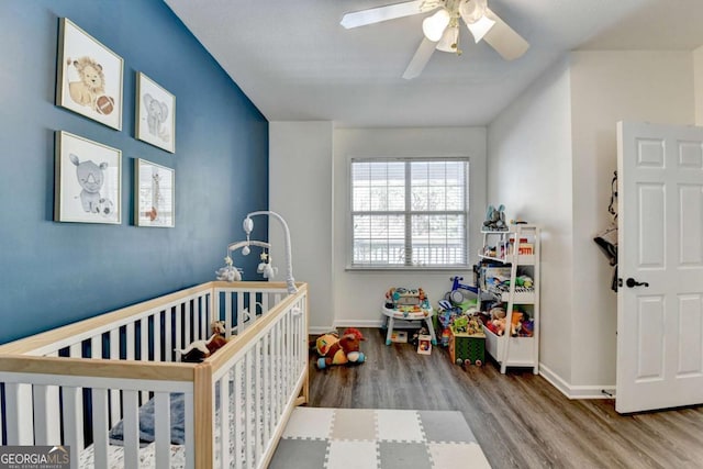 bedroom with hardwood / wood-style flooring, a nursery area, and ceiling fan