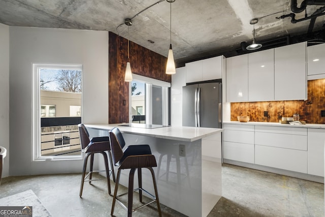 kitchen featuring stainless steel refrigerator, decorative light fixtures, white cabinetry, a kitchen breakfast bar, and black electric cooktop