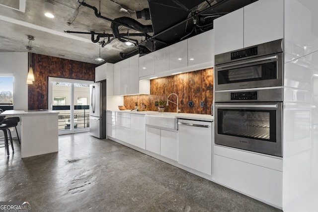 kitchen with pendant lighting, white cabinetry, sink, a kitchen bar, and stainless steel appliances