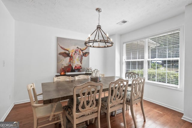 dining space with an inviting chandelier, a textured ceiling, and dark hardwood / wood-style flooring