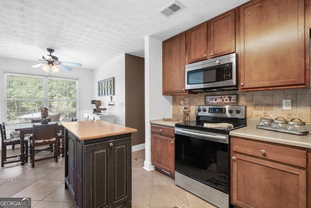 kitchen featuring appliances with stainless steel finishes, a center island, light tile patterned floors, and backsplash