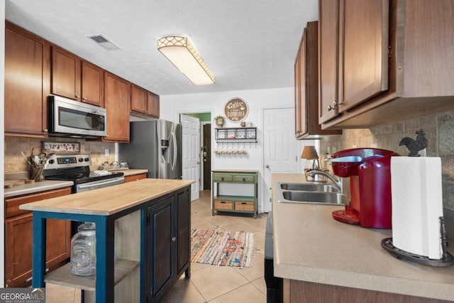 kitchen with appliances with stainless steel finishes, butcher block counters, sink, decorative backsplash, and light tile patterned floors