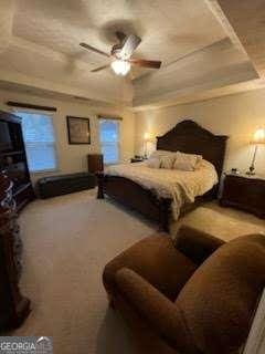 carpeted bedroom with a raised ceiling and ceiling fan