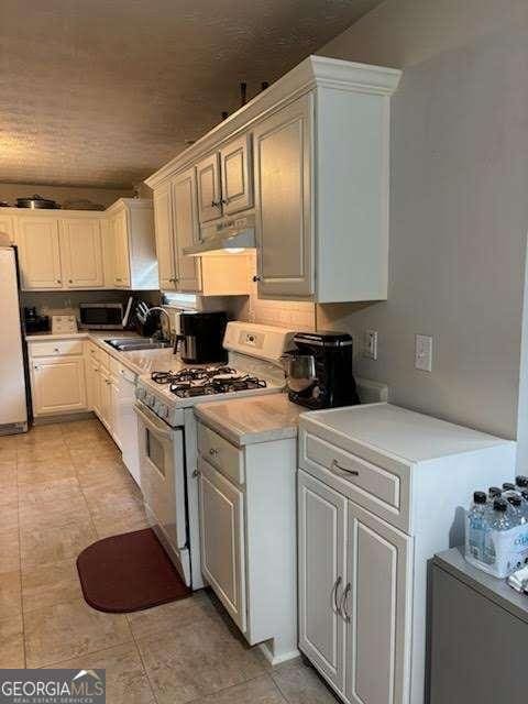 kitchen featuring white cabinetry, sink, light tile patterned floors, and white appliances