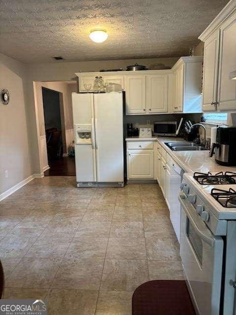 kitchen featuring sink, white appliances, a textured ceiling, and white cabinets