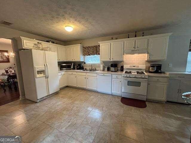 kitchen with sink, white appliances, tasteful backsplash, a textured ceiling, and white cabinets