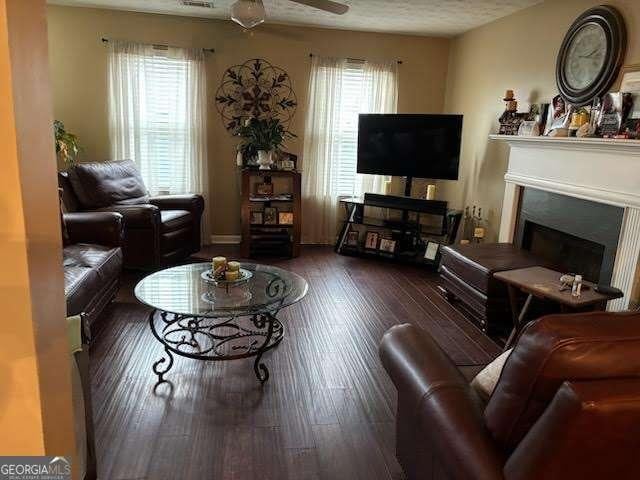 living room with a textured ceiling, dark wood-type flooring, and ceiling fan