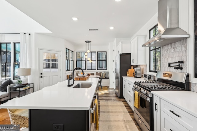 kitchen with sink, white cabinetry, appliances with stainless steel finishes, an island with sink, and island exhaust hood