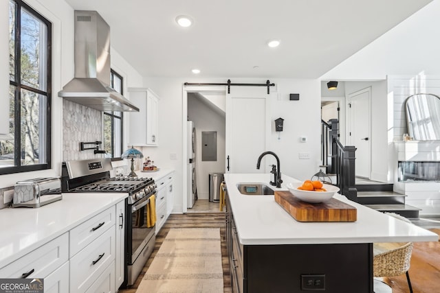 kitchen featuring sink, stainless steel gas stove, ventilation hood, a center island with sink, and a barn door