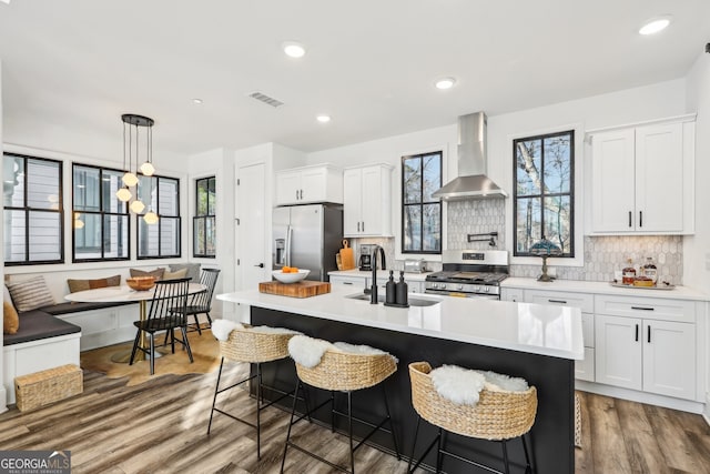 kitchen featuring breakfast area, white cabinetry, stainless steel appliances, and wall chimney range hood