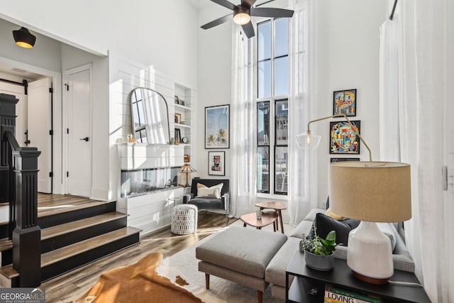 living area featuring ceiling fan, wood-type flooring, and a high ceiling