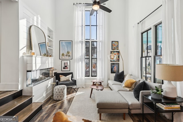 living area featuring a multi sided fireplace, a towering ceiling, ceiling fan, and dark hardwood / wood-style flooring