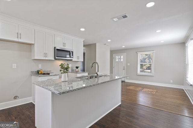 kitchen featuring sink, light stone counters, an island with sink, white cabinets, and dark hardwood / wood-style flooring