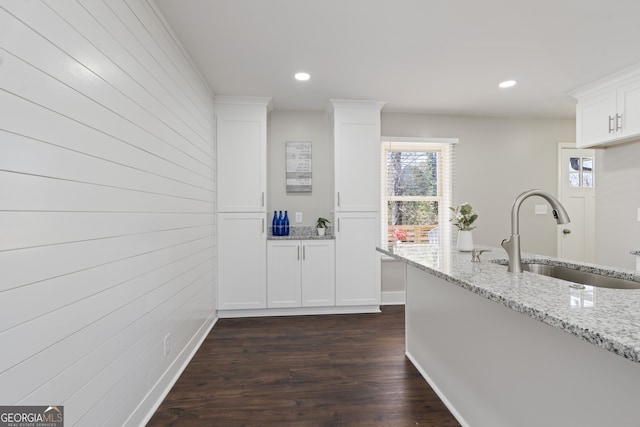 kitchen with dark hardwood / wood-style floors, wood walls, sink, white cabinets, and light stone counters