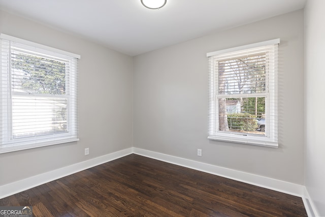 empty room with a wealth of natural light and dark hardwood / wood-style flooring