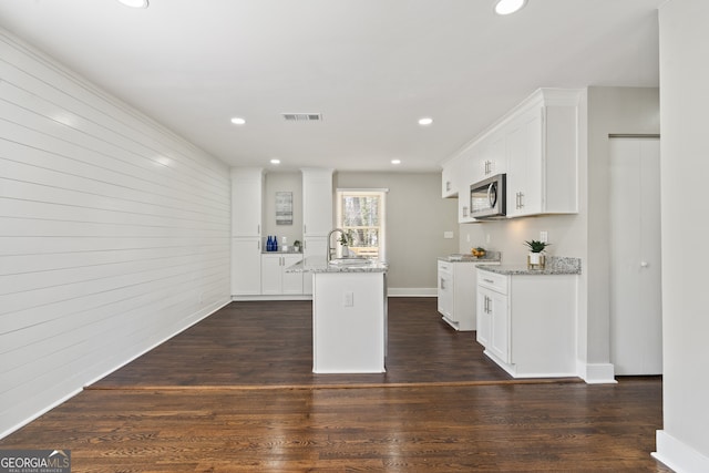 kitchen with white cabinetry, light stone countertops, and an island with sink