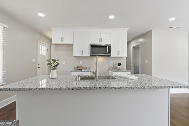 kitchen with light stone counters, a large island, sink, and white cabinets