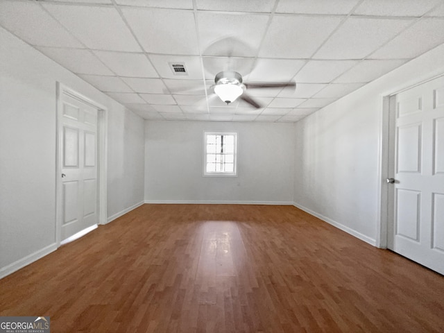 empty room with a drop ceiling, wood-type flooring, and ceiling fan