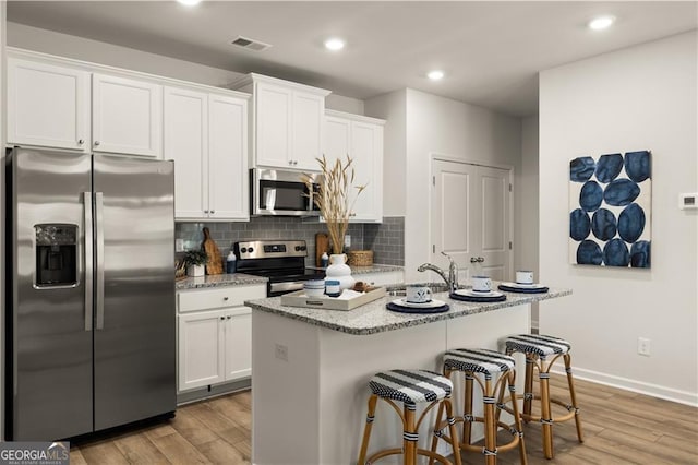 kitchen featuring white cabinetry, stainless steel appliances, light hardwood / wood-style floors, and a center island with sink