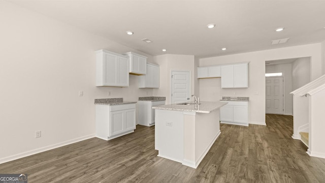 kitchen featuring a kitchen island with sink, sink, white cabinetry, and light stone counters