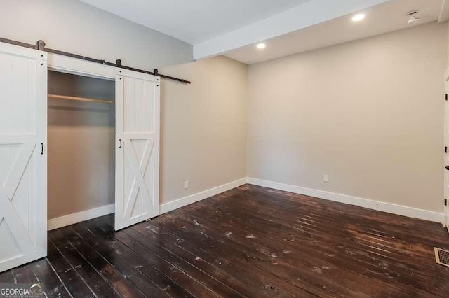 unfurnished bedroom with a barn door, dark hardwood / wood-style flooring, and a closet