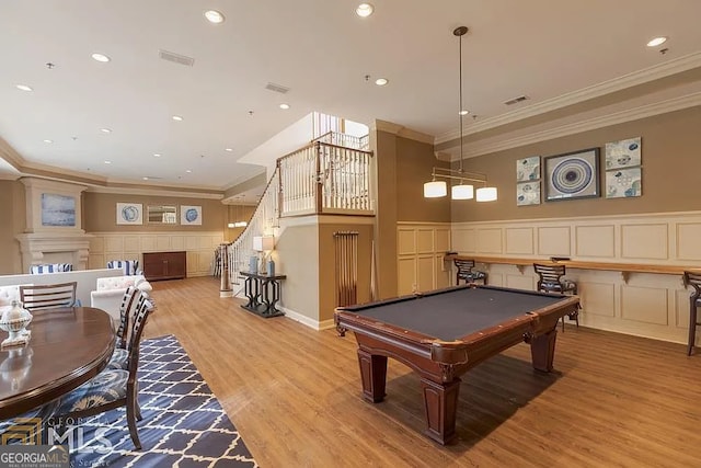 game room with light wood-style floors, wainscoting, a decorative wall, and crown molding